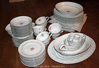 Assorted china pieces including dinner plates, salad plates, dessert plates, teacups, and saucers arranged on a wooden surface.