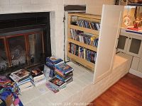 Photo showing DVDs and BluRay discs stacked near a brick fireplace and a wooden shelf with additional discs.