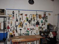 Wide view of assorted hand tools hanging on a pegboard wall including wrenches, crowbar, mallet, scissors, and work light.