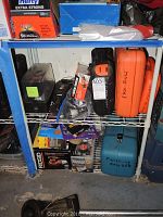 Shelf showing various power tools and their boxes including Ridgid drill, Skil jig saw in orange case, and Makita finishing sander in blue case.