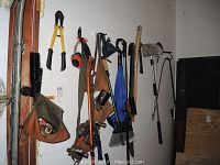 Photo of assorted hanging hand tools including bolt cutters, tool belt, hammer, and cleaning brushes