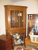 Front view of a large oak corner china cabinet with upper glass paneled doors and lower wooden cabinet doors open, showing dishware inside.