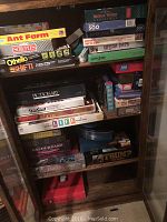 Shelf with stacked board games including Ant Farm, Scruples, Othello, Shift, puzzles by Springbok and others.