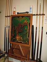 Full view of oak cue rack mounted on wall with cues on either side and items on top shelf