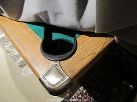 Corner of table showing oak-finish wood rail, green felt surface, and drop pocket with metal trim