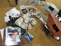 Overview of scattered vehicle parts, toy blasters, pamphlet, and photo prints on carpet