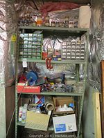 Overall view of grey metal shelving containing various hardware storage boxes, jars, and supplies