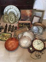 Overview photo showing silver platters, framed paintings, carved wooden bowl, clock and some hanging decor pieces laid out for display.