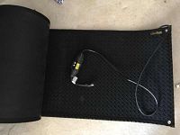 Photo showing the rolled out black heavy duty textured floor mat with attached power cord.