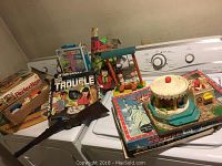 Full view of toy collection on washer including board games, toy rifle, and various colorful vintage toys
