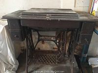 Full view of vintage Singer sewing machine mounted inside a wooden cabinet with drawers on sides, showing wear and rust.