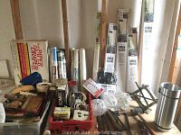 Overview photo showing packaged mini blinds, hand tools, lightbulbs, and rolls of paper on a table
