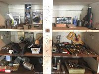 Wide view of shelves with assorted tools, saws, and hardware items arranged. Includes hand tools, cordless drill, and various small tools and components.