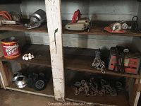 Wooden cabinet with bottom three shelves visible; shelves contain various tools and items including a coffee tin, solar lights, and chains.