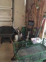 Photo showing black wheelbarrow with wooden handles, bags of soil and fertilizer in the background, metal garden stands, and green metal garden wagon.