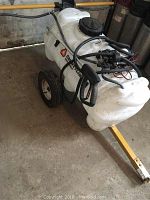 Wide view of white chemical sprayer unit showing tank, hose, and metal frame with wheels.
