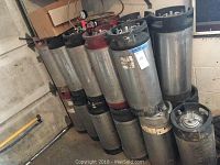 Multiple stainless steel Cornelius kegs stacked in a basement corner