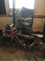 Red road bike and two lawnmowers shown in garage with concrete walls and basement window.