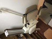 Full view of stair lift mounted on carpeted stairs showing chair and track