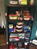 Full shelving unit with multiple kitchen paper products and disposable items including cups, pans, wipes, plates, storage containers, and jugs.