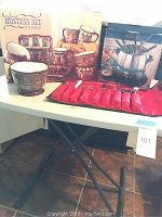 Photo of the folding table supporting the 12-piece hostess set box, fondue set box, ceramic bowl, and red utensil pouch on top.
