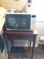 Microwave oven on the wooden end table with some decorative items on top, showing size and condition