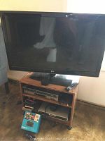 LG 44-inch TV on top of wooden TV stand with visible components and remote.