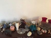 Shelf display of assorted vases, bowls, and figurines including red glass vases, blue vase, clear bowl, pink container, and animal figurines.