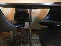 Photo from below the table showing the base and seats of the four black leather swivel chairs.