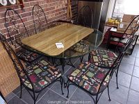 Full view of table with six chairs around a round glass top table showing the patterned cushions on chairs and metal ornate backs.