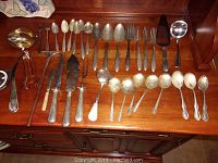 View of all 30 pieces including forks, knives, spoons, serving spoons, and other cutlery laid out on wooden surface.