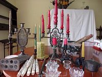 Wide view of the collection on a wood table including candelabras, several candlesticks, decorative candles, and a metal candle mold.
