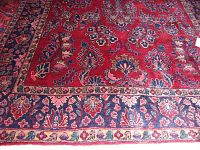 Close-up of rug corner showing red field with floral motif and outer navy blue border