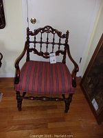 Front angle showing carved wood details, spindle back, armrests, turned legs, and striped upholstery