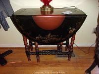 Full view of the table showing closed drop-leaf top, black and reddish-brown paint with Asian motif landscape design.
