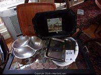 Set of assorted metal trays including black tray with image and divided metal serving dish on glass table with floral patterned fabric underneath