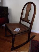 Front left side view of the cane-seat wooden rocking chair showing cane seat, wood frame, and leg details.