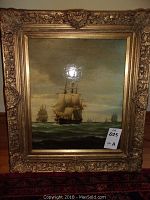 Photo showing entire framed ship-themed oil painting with ornate gold frame on a floor against a wall.