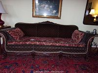 Full front view of sofa showing dark brown diamond pattern upholstery, red-patterned cushions, carved wood frame and legs.