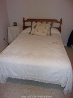 Full view of full size bed with white bedspread, mattress and decorative pillows on carpeted floor.