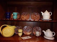 Shelf display showing paisley dishes, teapots, pitcher, and mugs in various colors.