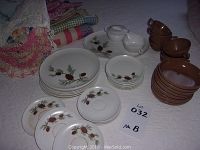 Photo showing melamine dishes with pine cone pattern: plates, saucers, cups, bowls arranged on a surface.