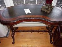 Top view of kidney-shaped table top with dark worn leather-like surface and carved wooden edge