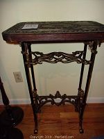 Front view of accent table showing carved wood top and decorative metal base.