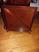 Photo of the planter box showing the decorative X-panel and carved feet on one side, placed on hardwood floor.