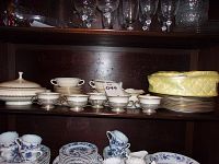 Shelf view showing various Lenox ivory and gold leaf trimmed china pieces including pedestal cups, plates, and serving bowls.