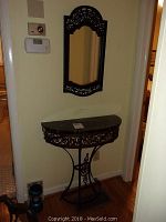 Hall table with mirror photographed in hallway, showing overall view of table with marble top and metal base and matching metal framed mirror on wall