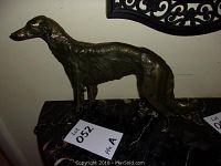 Front and side view of dark bronze-colored cast metal dog figurine standing on a black surface.