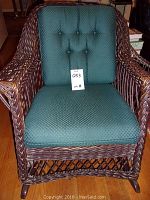 Front view of wicker rocking chair with green tufted cushions and lot tag on seat