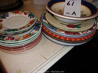 Stack of assorted plates and bowls featuring fruit and floral motifs including cherries, apples, and leaves with borders in multiple colors.